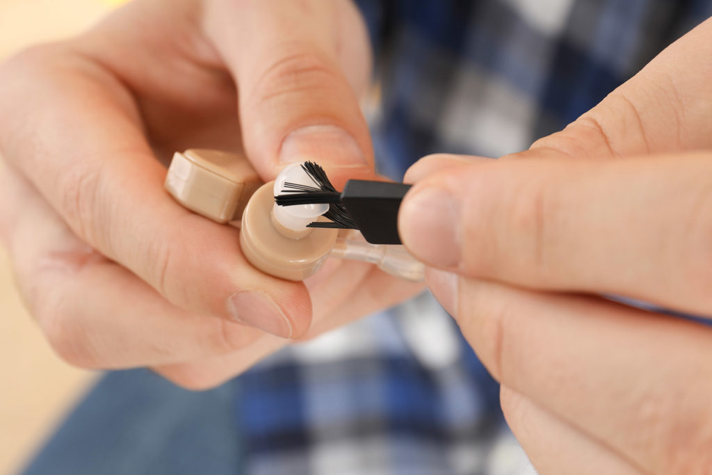 hands gently brushing debris from hearing aid device